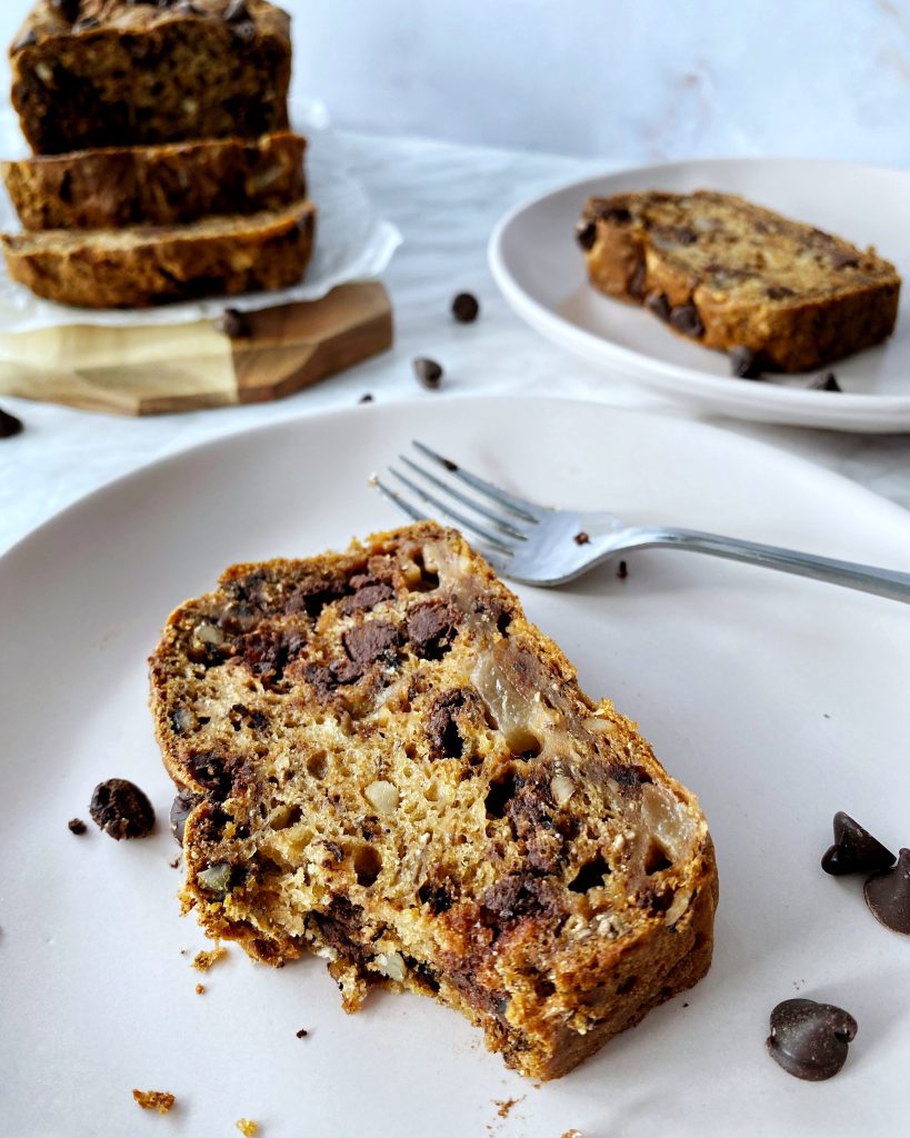 slice of vegan sweet potato pear loaf in a pink plate with loaf in the background