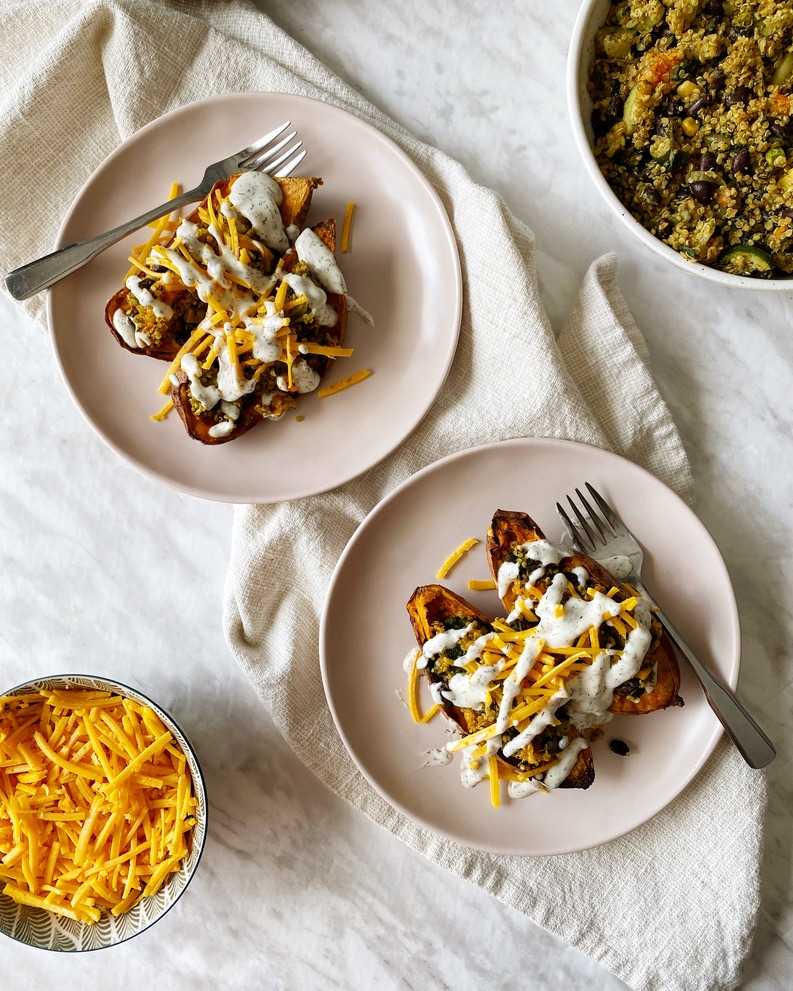 two plates of quinoa stuffed sweet potatoes topped with cheese and mayo dressing