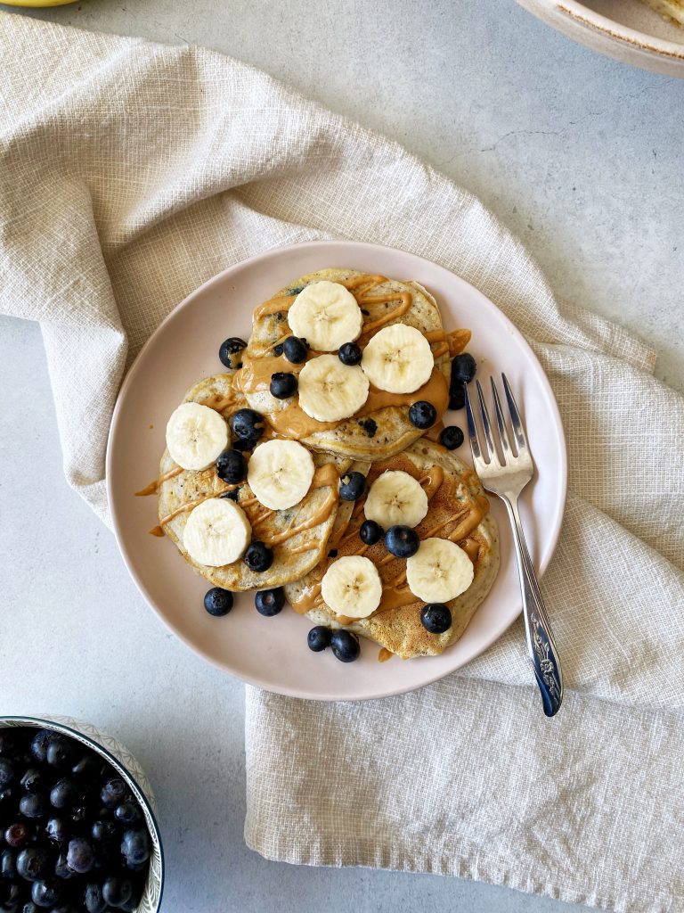 blueberry vegan pancakes topped with bananas and blueberries on a pink plate