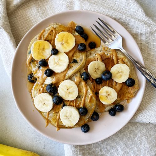 fluffy vegan blueberry pancakes topped with bananas blueberries and maple syrup