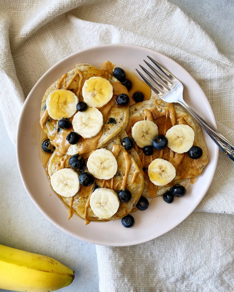 fluffy vegan blueberry pancakes topped with bananas blueberries and maple syrup