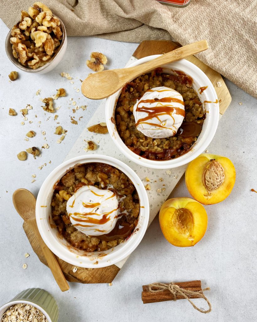 overhead shot of two peach crisps in a ramekin topped with ice cream and caramel drizzle