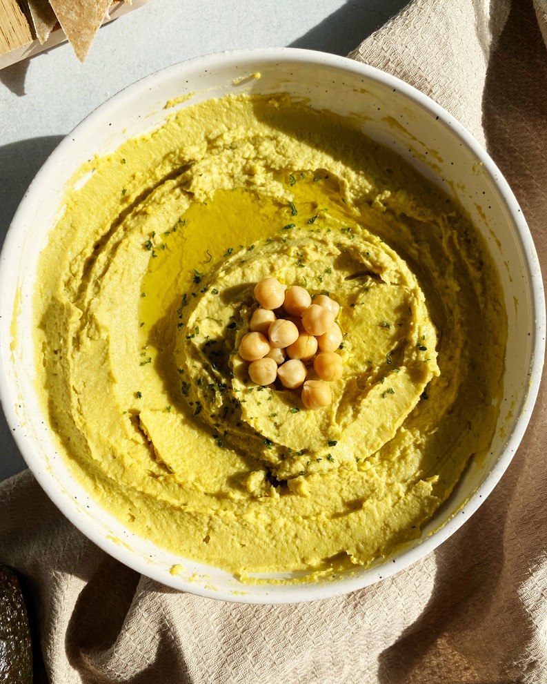 creamy vegan avocado hummus in a bowl topped with olive oil, parsley, and extra chickpeas