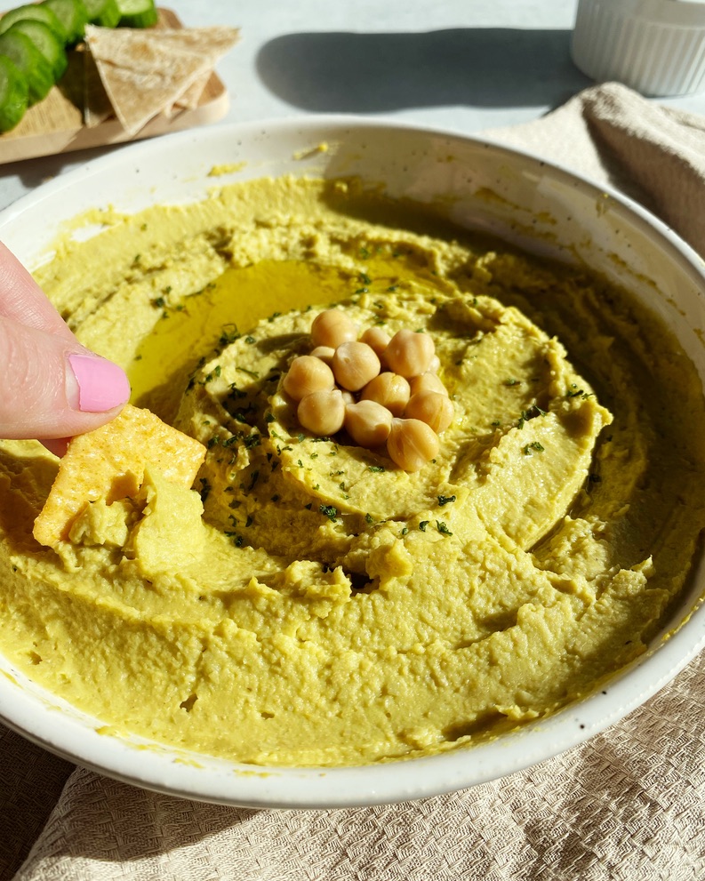 cracker being dipped in creamy avocado hummus