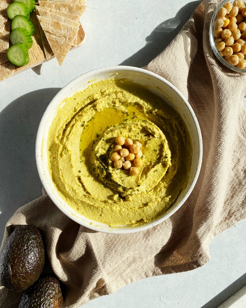 creamy avocado hummus in a small bowl topped with olive oil and extra chickpeas in the sunlight