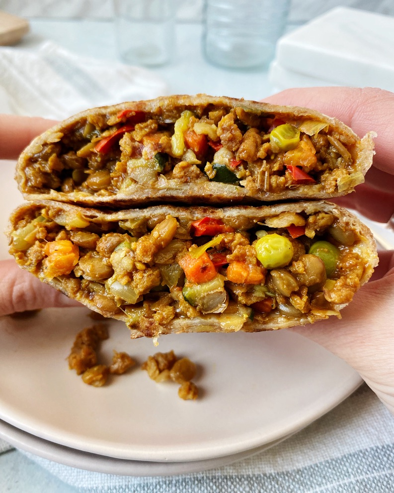 two hands holding up vegan burrito cut in half to show the center
