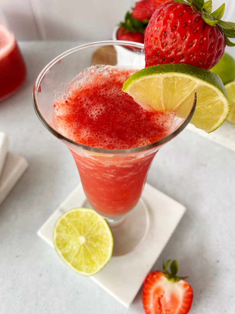close up of the top of the strawberry daiquiri glass showing the drink and lime wedge with a cut strawberry
