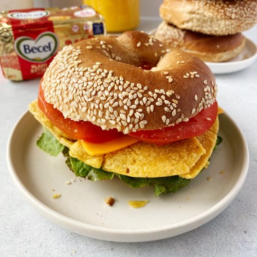 vegan breakfast bagel filled with a vegan omelette, lettuce, tomato, and vegan cheese