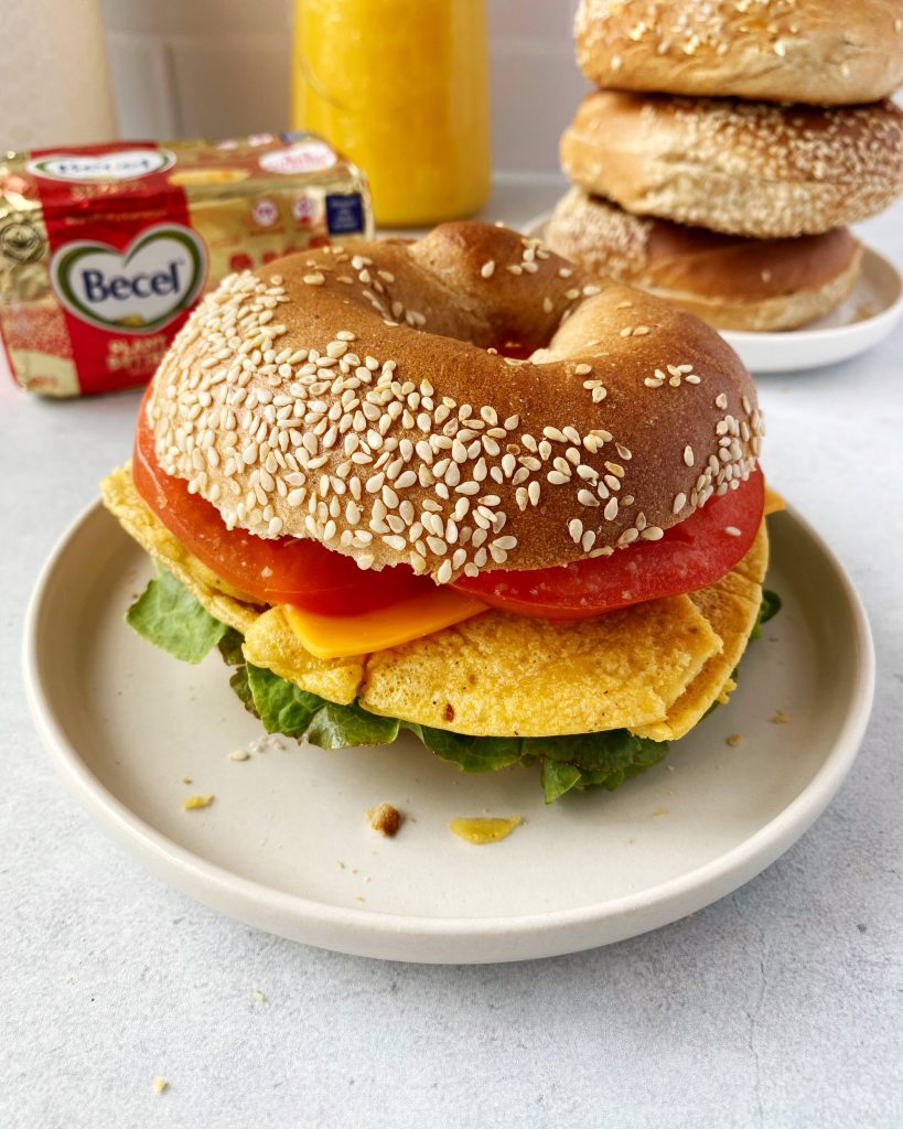 vegan breakfast bagel filled with a vegan omelette, lettuce, tomato, and vegan cheese