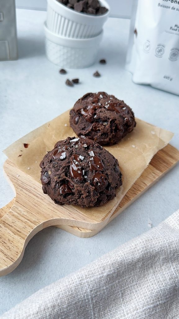 two chocolate protein cookies on a small wooden board