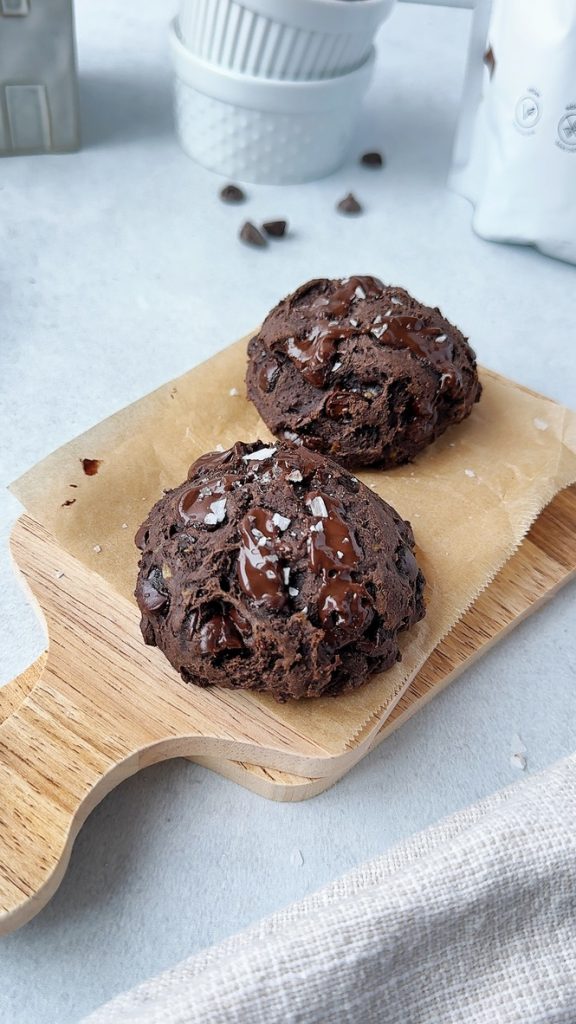 two chocolate protein cookies on a small wooden board