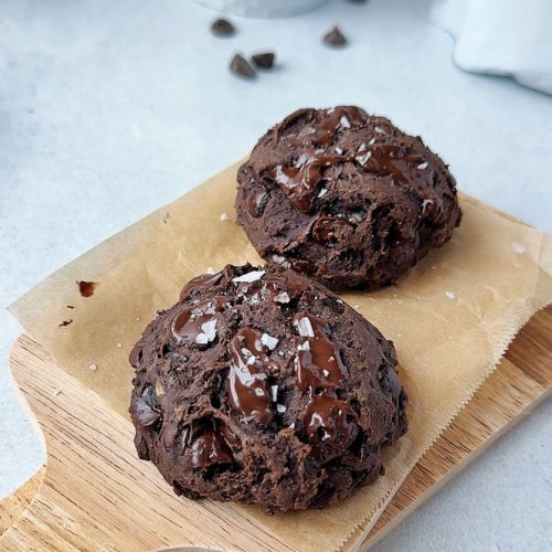 two chocolate protein cookies on a small wooden board